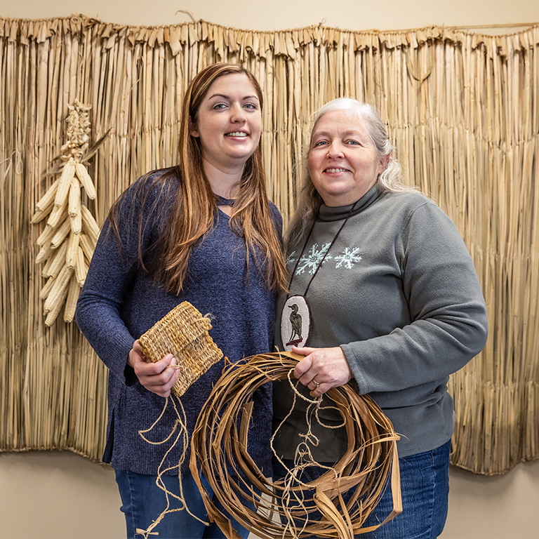 Two people pose for photo with natural weaving supplies. 